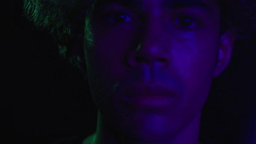 A young man is crying as blue lights flash across his face in the dark