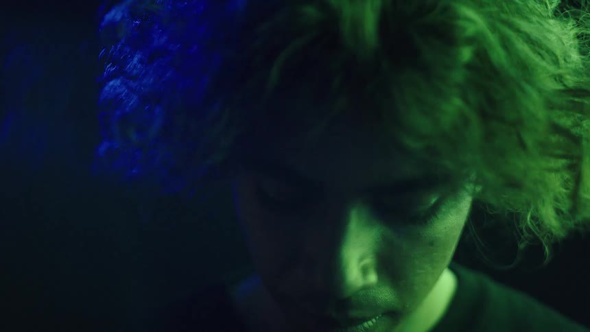 Young face tilted downward under soft blue light