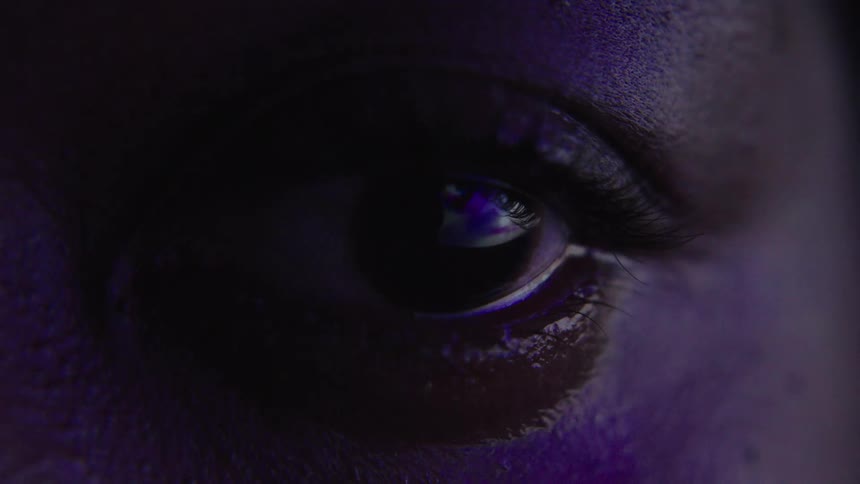 Closeup eye lit by intense purple light in the dark