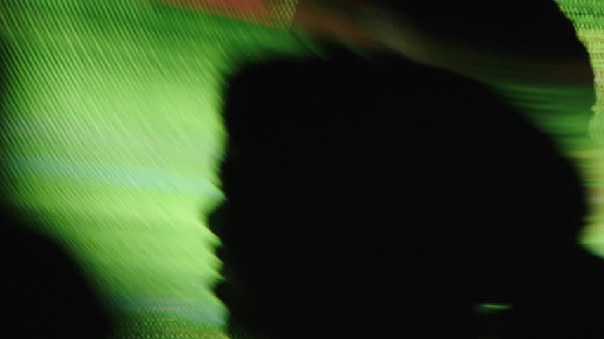 A silhouette of a woman is shown in profile with her head and shoulders visible against a background of flashing and shifting lines of green magenta and blue light