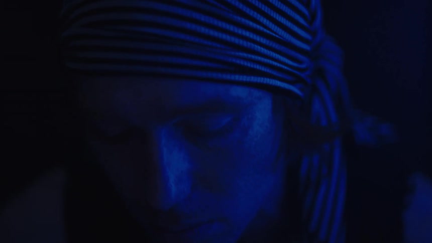 Man with a striped bandana is illuminated by intense blue light