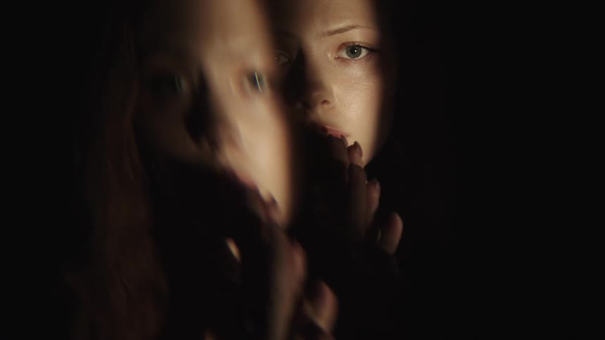 Woman with a serious expression reflected in a mirror lit by a strip of light