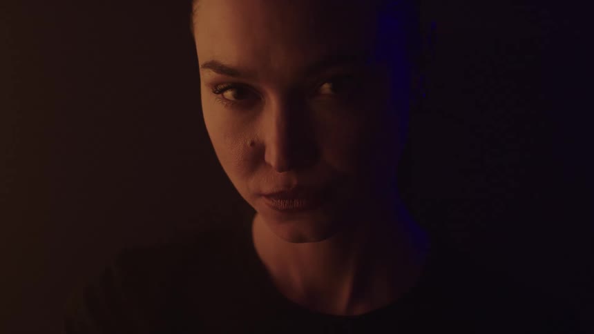 Woman stares intensely under warm lighting and deep shadows