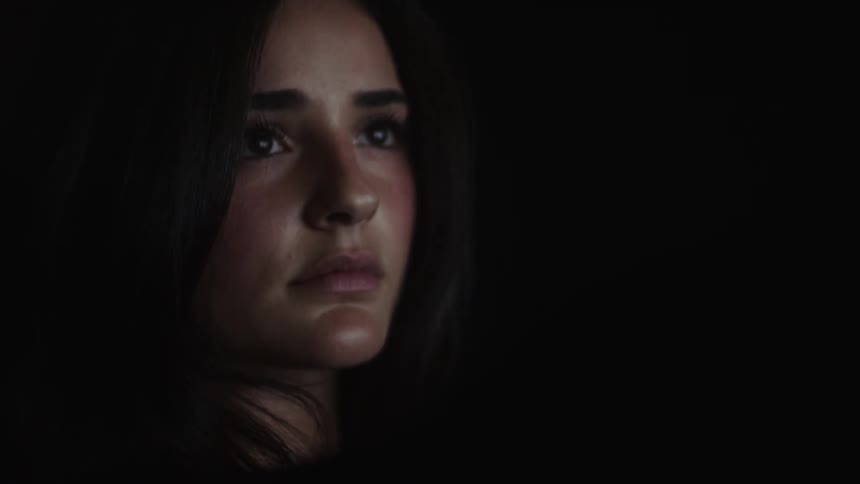 The video shows a closeup shot of a woman with dark hair and a light shirt her expression is somber with her head tilted slightly downwards