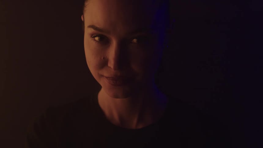 A young woman in a dark room wearing a black tshirt shows a hint of happiness