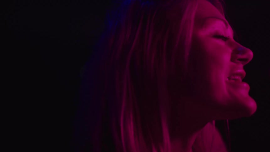 Smiling woman lit by pink and purple lights in a dark setting