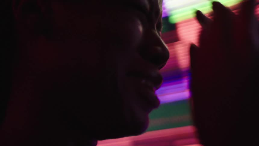 The video shows a person in profile silhouetted against a bright colorful screen that displays what looks like data streams or code the person is looking up and moving as if dancing to the music
