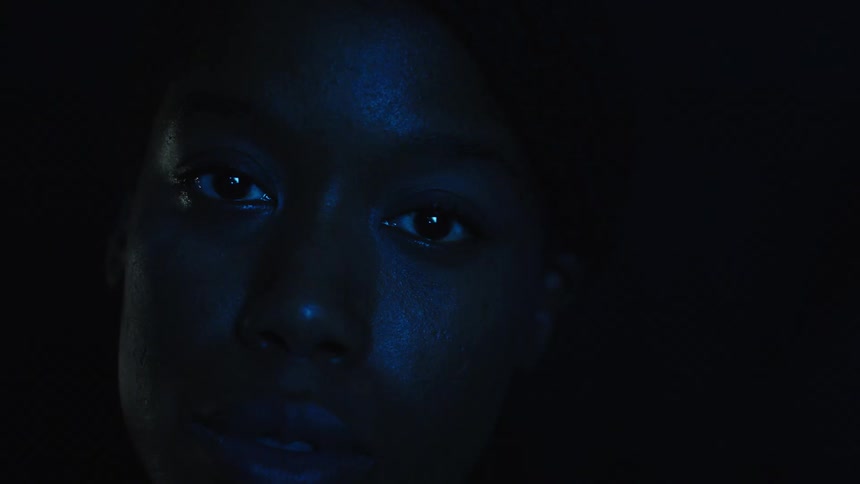 The video shows a persons face in a dark room illuminated by a pulsing blue light that shifts and changes their eyes are visible as they look around