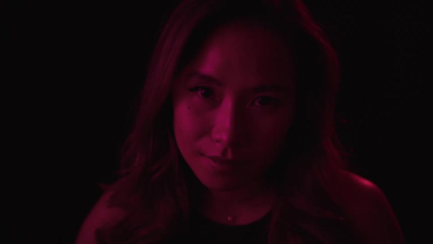 A womans face illuminated by a deep red light as she stares intensely at the camera