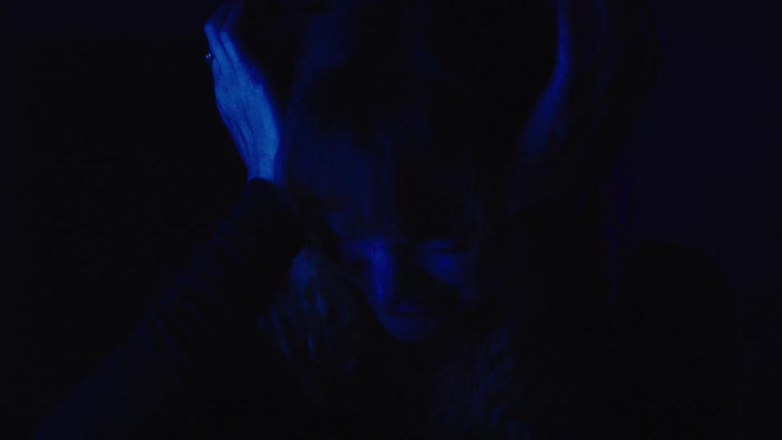 A woman in a dark room filled with sadness bursts into tears as the space is illuminated by dark blue light