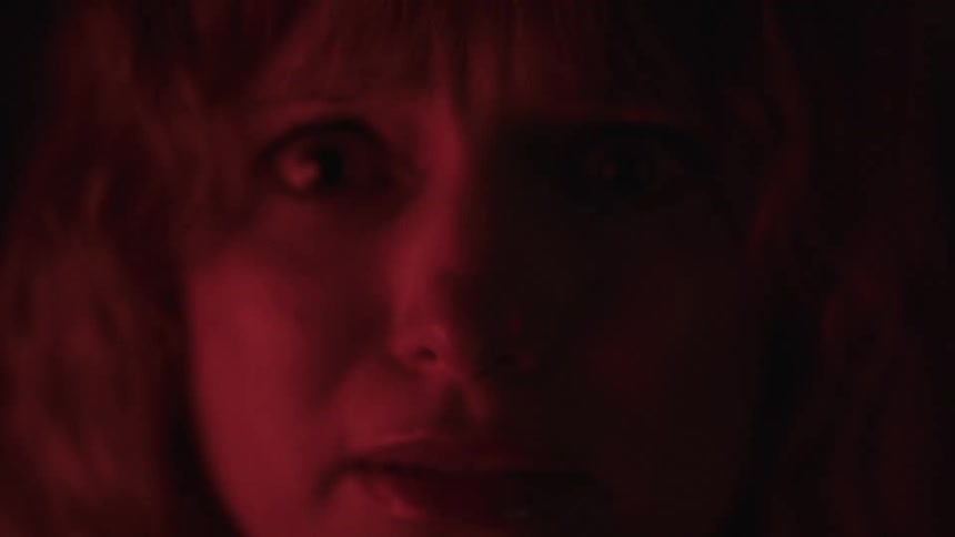 A scared woman in the dark with red light falling on part of her face