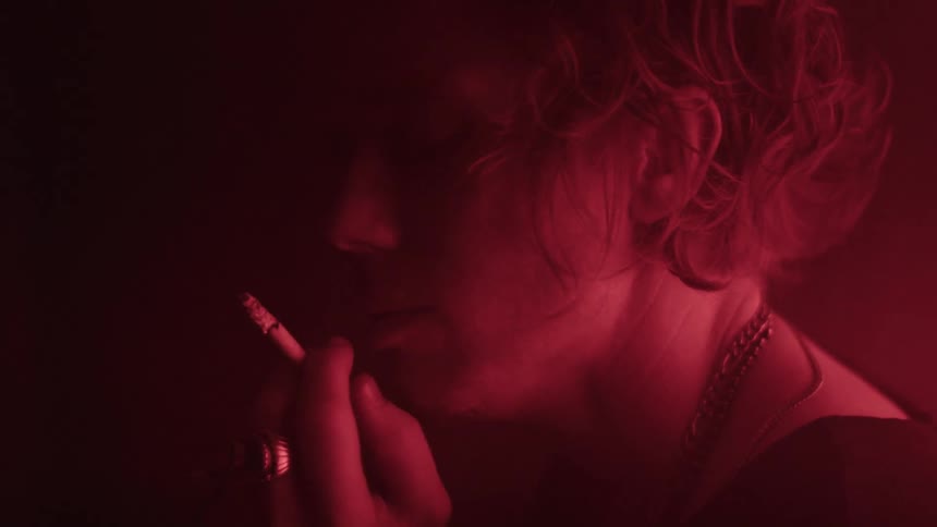 A woman smokes a cigarette inside a dark room illuminated by red light