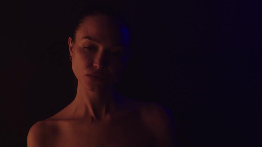 Woman with bare shoulders in a dark setting softly lit with orange and blue tones