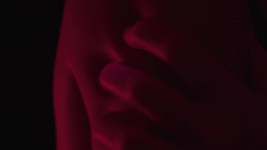 A hand massages a persons back dragging the skin inside a dark room illuminated by red light