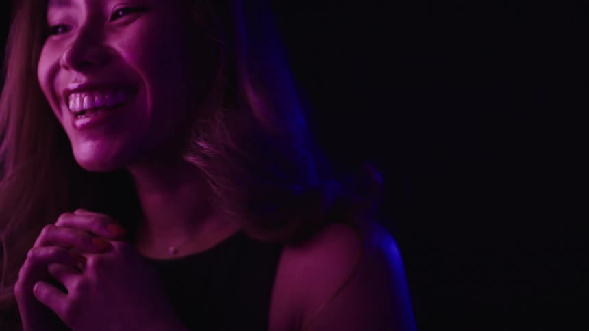 A woman smiles and moves her head dramatically under colored light