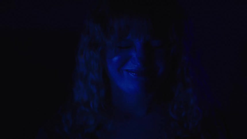 A sad woman is illuminated by a blue light in a dark room