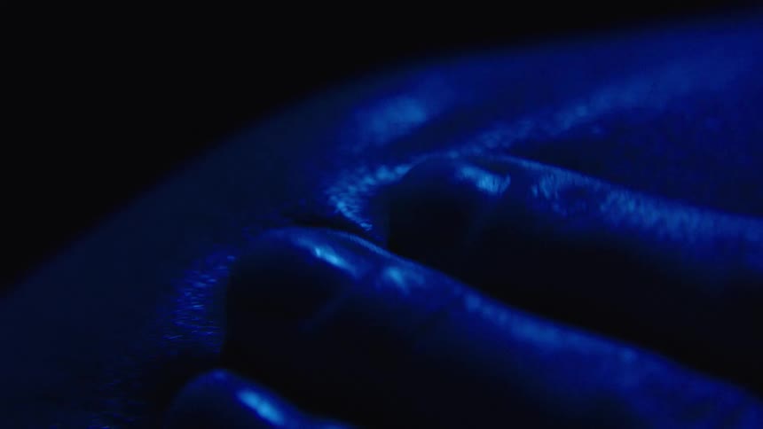 A close view shows a persons hand passing over skin with a glowing blue light moving across it highlighting the textures of their skin and fingers