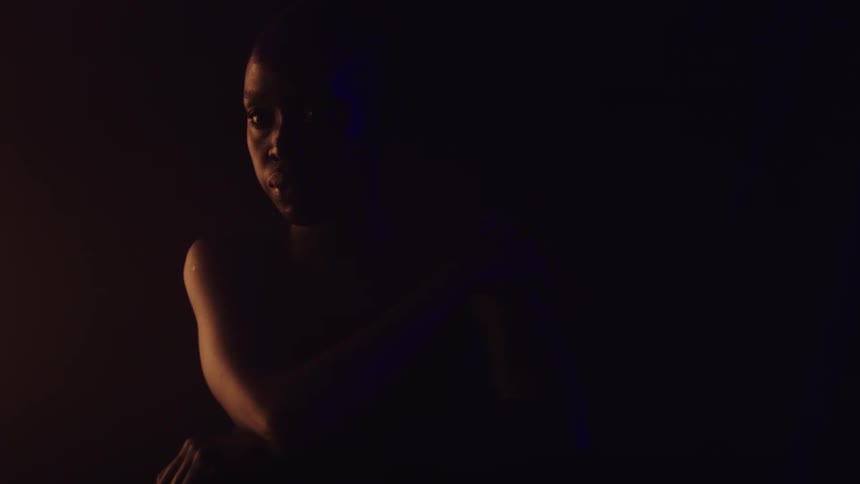 A young woman sits indoors in a dark room