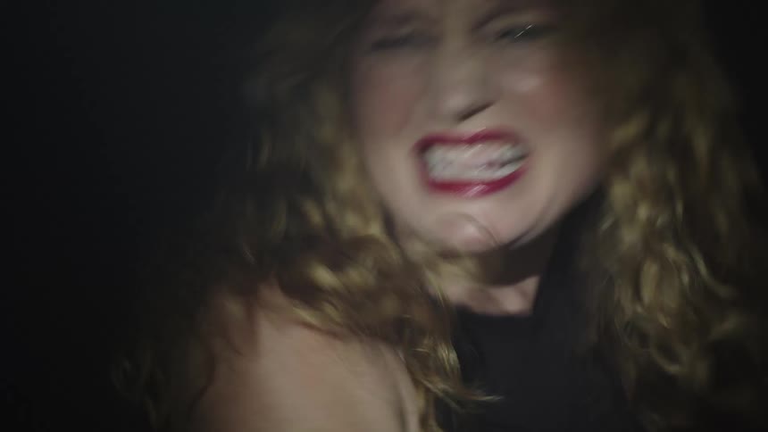 A young woman filled with rage moves chaotically and angrily inside a dark room as the light flickers