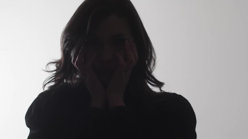 A woman holds her face in shadow against a bright white background