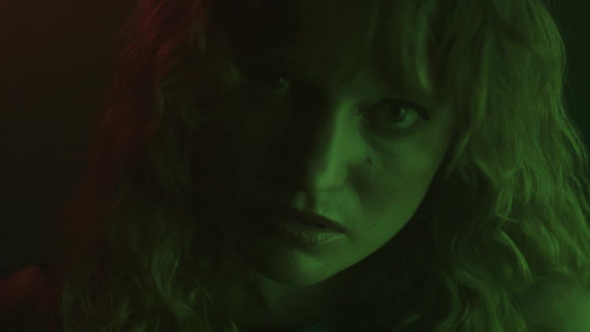 A closeup of a womans face is shown in a dark room with green and red lighting while she is changing her expression