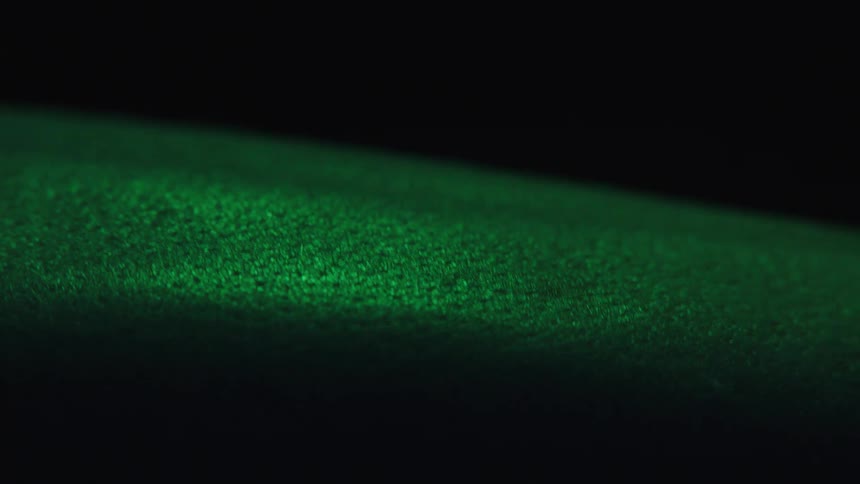Light creates highlights on a green fabric moving in a dark area