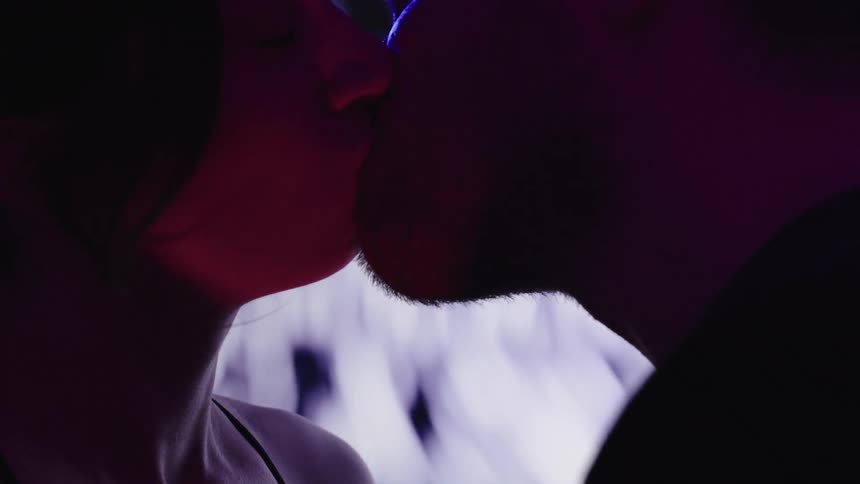 Couple kisses while a blurry pattern swirls on a screen nearby