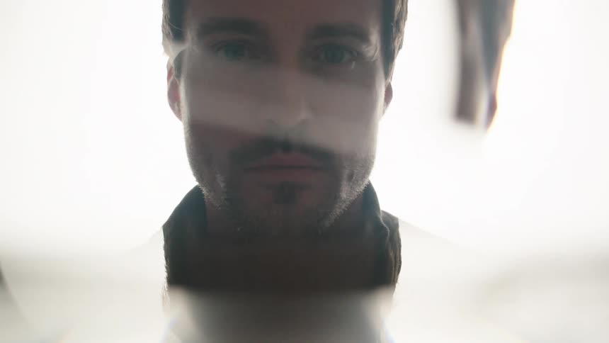 Bearded man staring intently through a bright opening