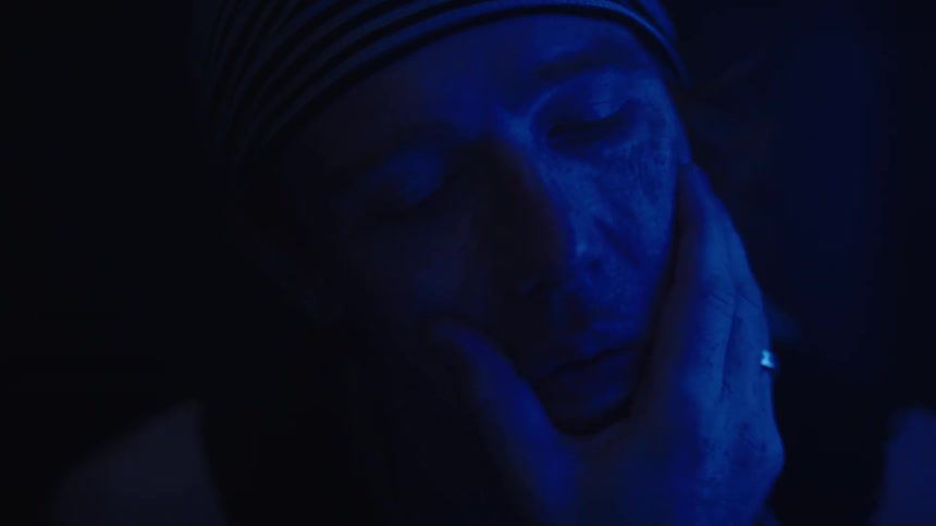 Man with closed eyes has his face held by a hand under blue light