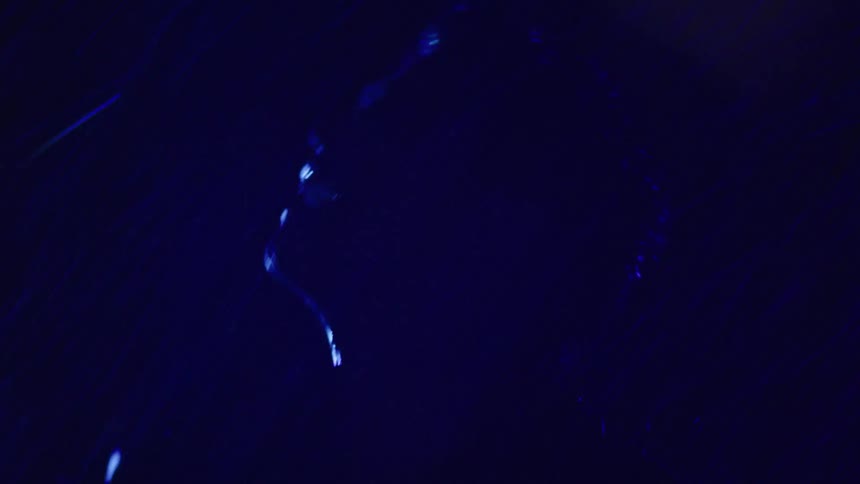 Shadowed silhouette appears under intense blue lighting in the dark at night in the rain