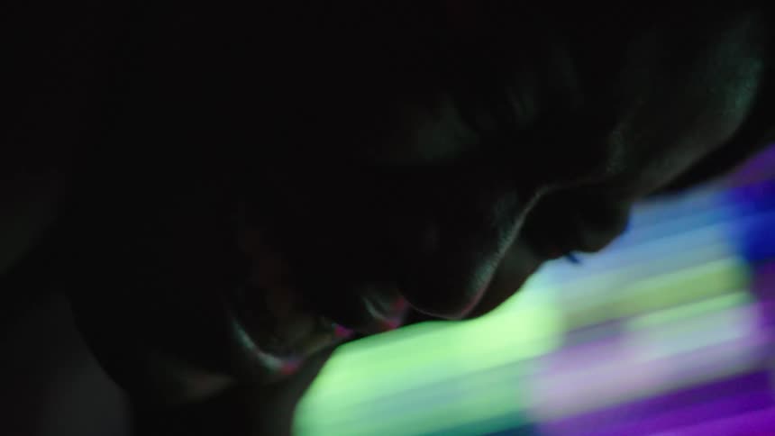 The video shows a dark scene that is suddenly illuminated by a pulsing vibrant pink and purple light a persons profile is visible illuminated by the light