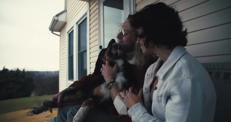 Couple on the porch receiving affection from their dog