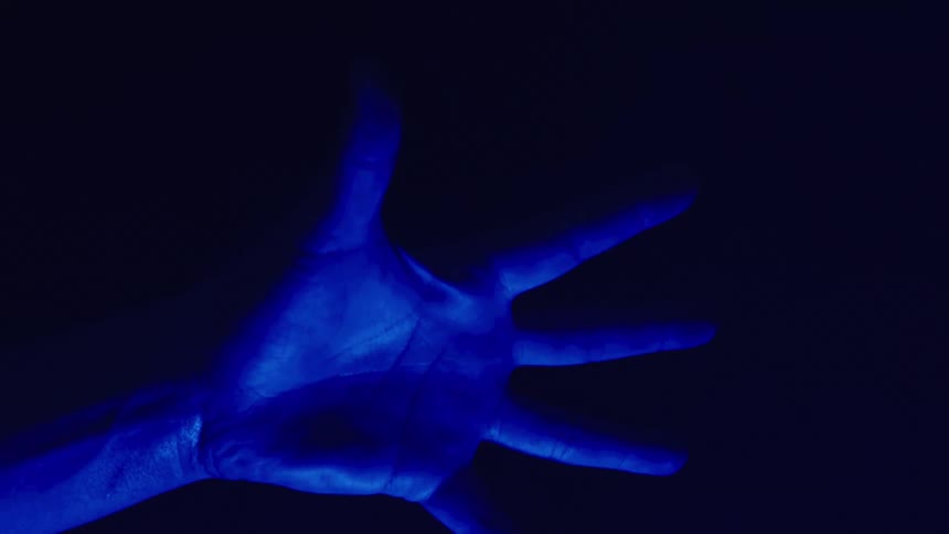 A person opens and closes their hand as it is illuminated with blue light