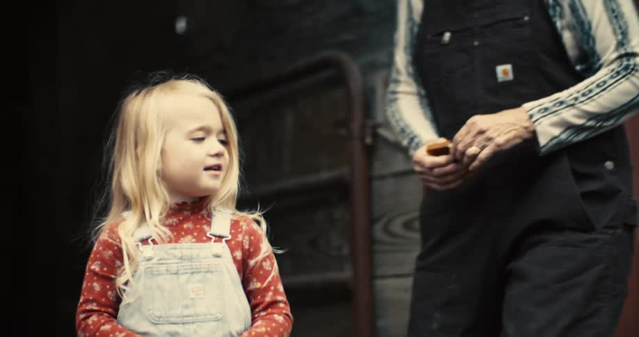 Child in light overalls stands in front of an adult wearing black overalls