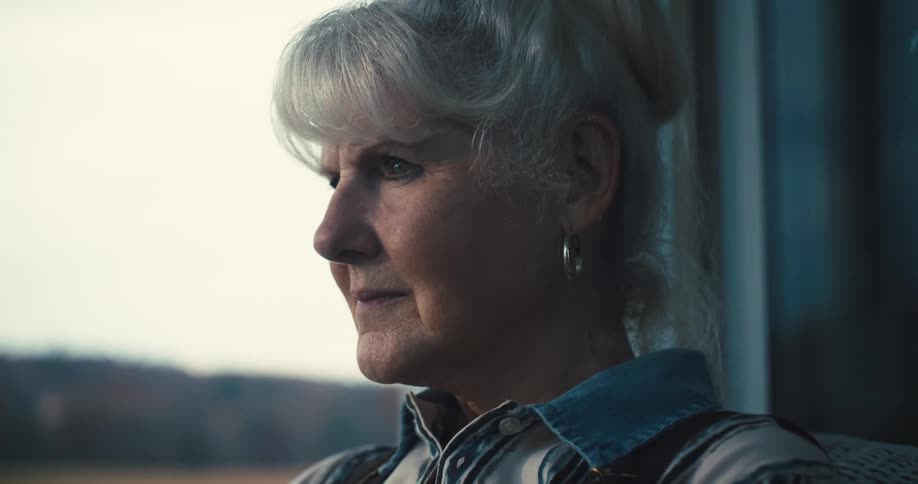 Based on the images from the video a closeup profile of an elderly woman with short gray hair is shown she is wearing a collared striped shirt with what looks like brown suspenders the woman is looking off into the distance and the background is a