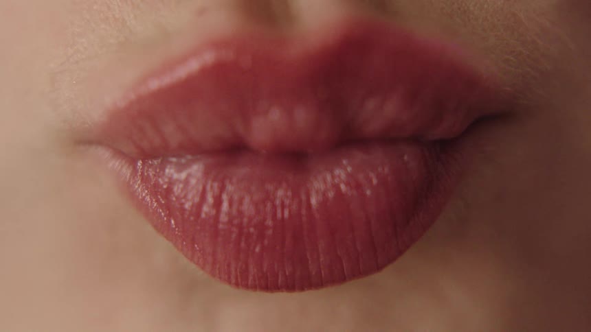 Closeup on lips painted with red lipstick forming a kiss pout
