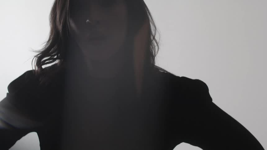 The video shows a persons silhouette against a bright white background they are seen from the side then they turn to face the camera before turning back to the side and walking away