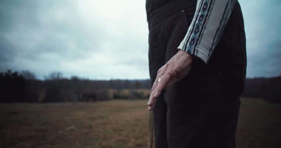 A closeup lowangle shot focused on the hand of an elderly person showing the wrinkles and prominent veins as it rests on a wooden fence post in a rural outdoor setting