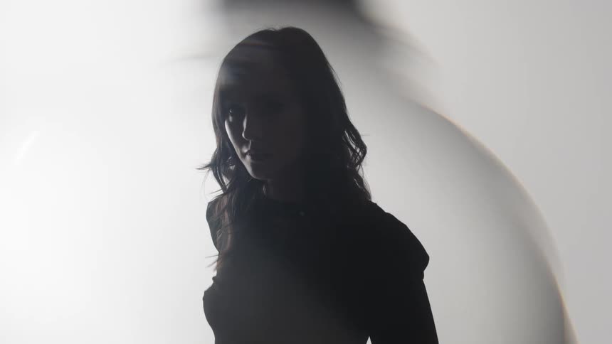 Woman in partial silhouette appears in a scene lit by diffused light