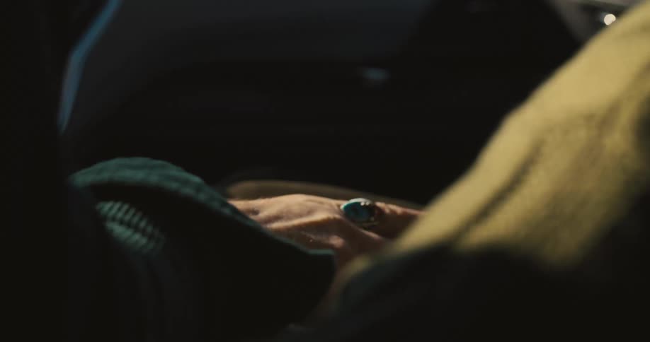 A closeup of two hands clasped together inside a moving car with soft sunlight over them
