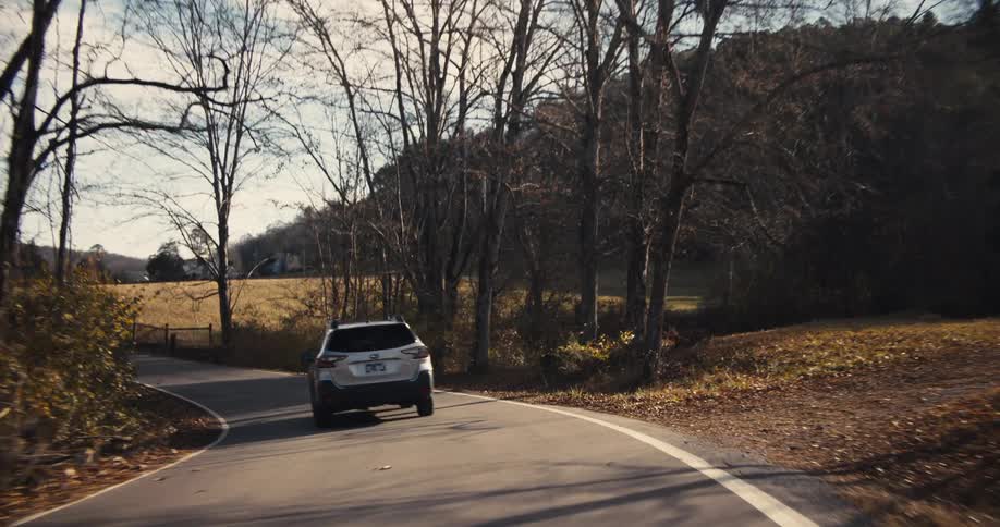 Car driving on remote country road passing through trees and open fields