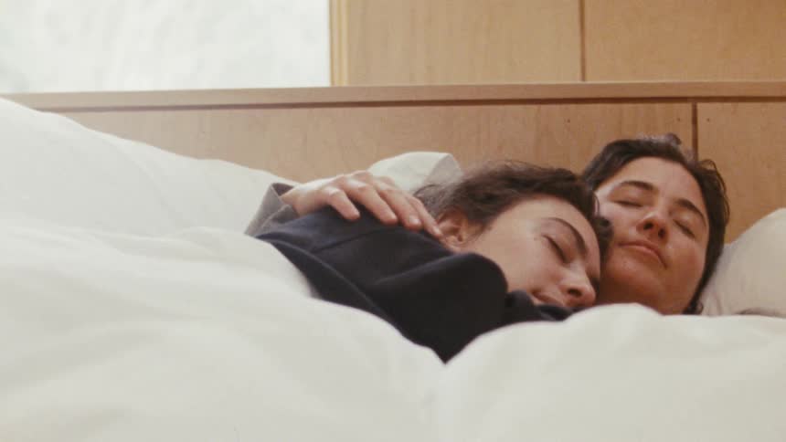 A couple cuddles under a blanket while sleeping in their bed at sunrise smiling in their sleep
