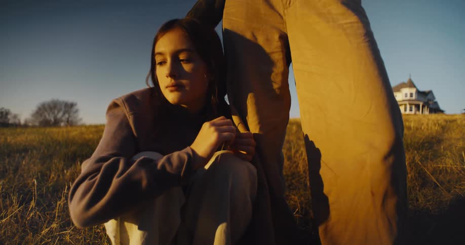 A teenager is sitting in the grass by a woman