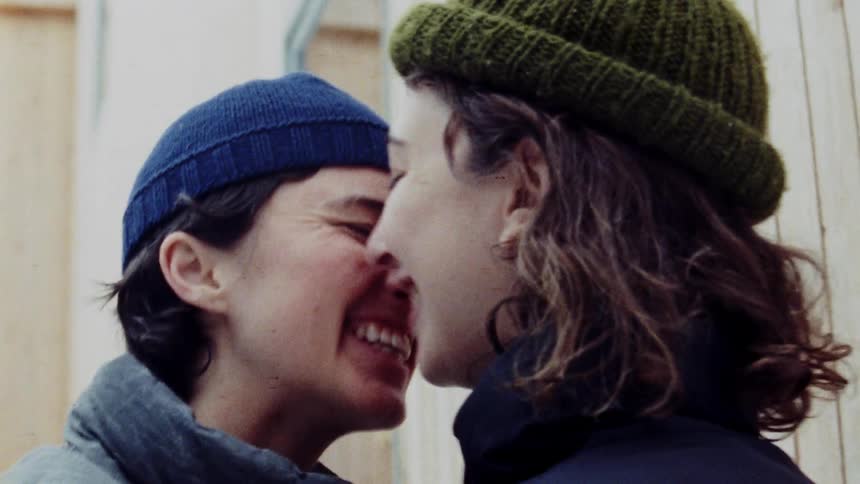 Two women smile and kiss outside