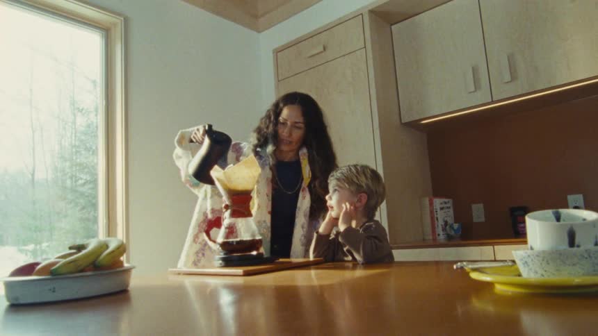 A woman and a child are standing in a kitchen as the woman pours water into a pourover coffee maker