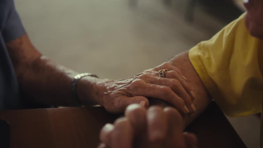 Elderly hands intertwined on the table in a gesture of affection