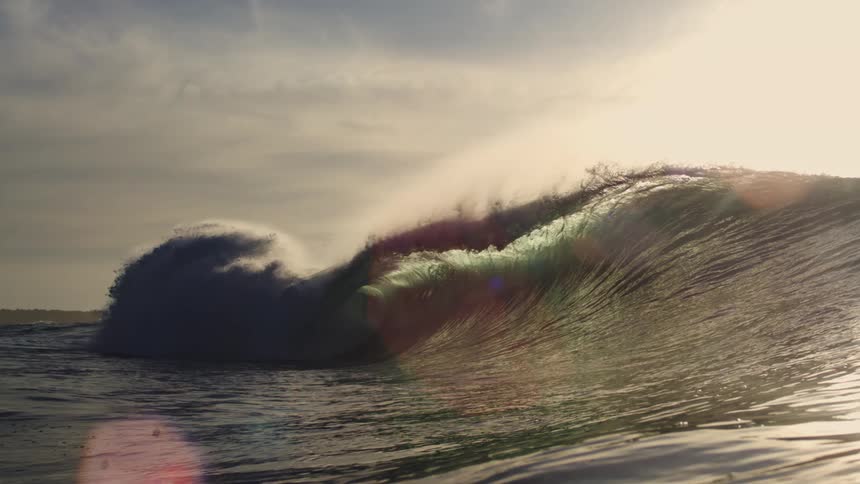 A powerful ocean wave curls at sunset