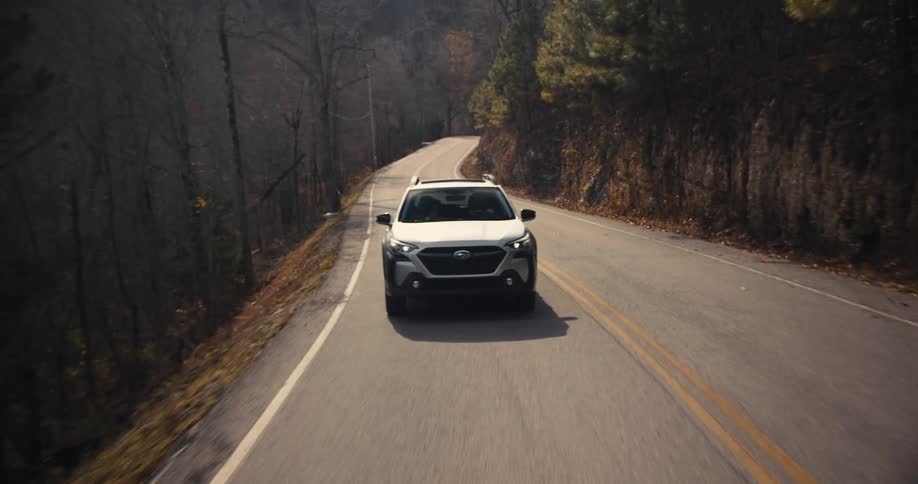 A white suv drives along a winding twolane road bordered by rocky slopes and sparse trees