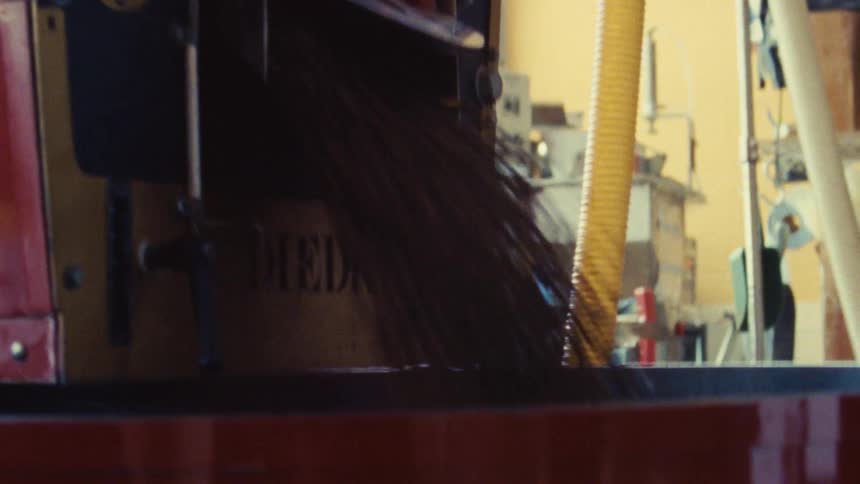 The video shows a closeup of a persons hand turning a crank on a red and black industrial machine the machinery appears to be a coffee roaster and the hand is moving a lever to agitate the beans