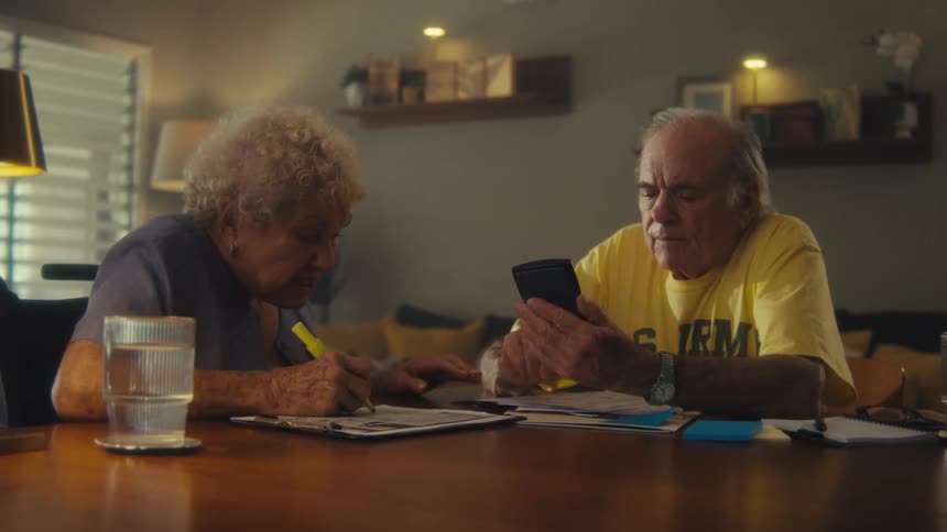 An elderly couple works on paperwork using a smartphone